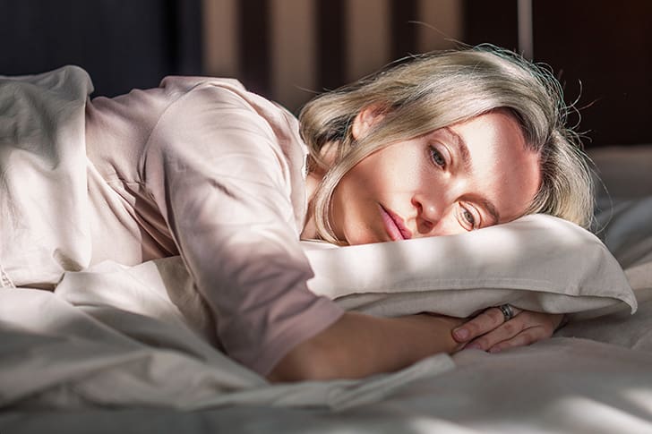 A woman lies in bed, showing the importance of sufficient sleep for metabolic health and weight loss—key principles behind HLTH Code Complete Meal.
