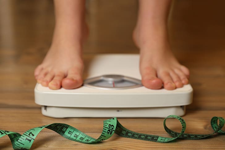 Bare feet on a bathroom scale beside a measuring tape, symbolizing progress in weight loss through healthy nutrition and balanced habits.