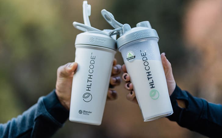Two hands clinking HLTH Code Complete Meal shaker bottles, symbolizing shared commitment to metabolism health and lasting weight loss.