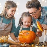 Family carving a Halloween pumpkin together, celebrating the holiday season and exploring the joyful origins of Halloween and Christian holidays.