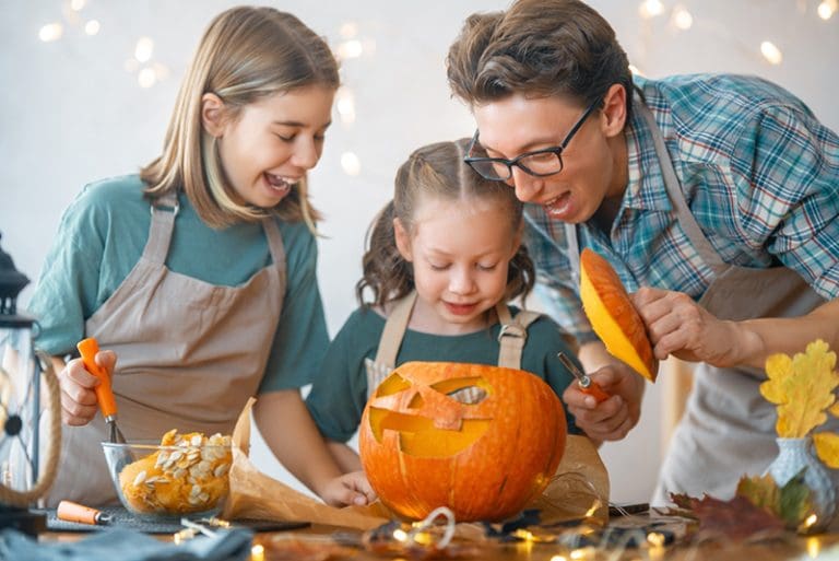Family carving a Halloween pumpkin together, celebrating the holiday season and exploring the joyful origins of Halloween and Christian holidays.