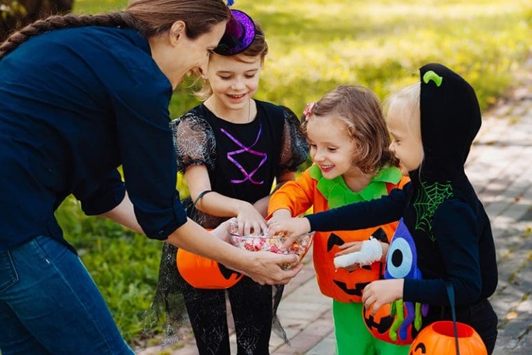 Children in Halloween costumes collecting candy from a woman on Halloween night — a heartwarming Halloween story of trick-or-treaters and joy.