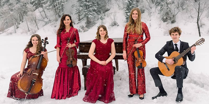 Jenny Oaks Baker and her children, Family Four, pose in elegant red attire with their instruments on a snowy mountain backdrop, promoting Joy to the World! A Sacred Celebration from the Jenny Oaks Baker Christmas Tour 2025.