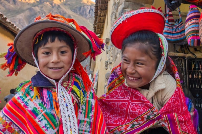 Peruvian children in traditional Quechua dress smiling together in Ollantaytambo, Peru