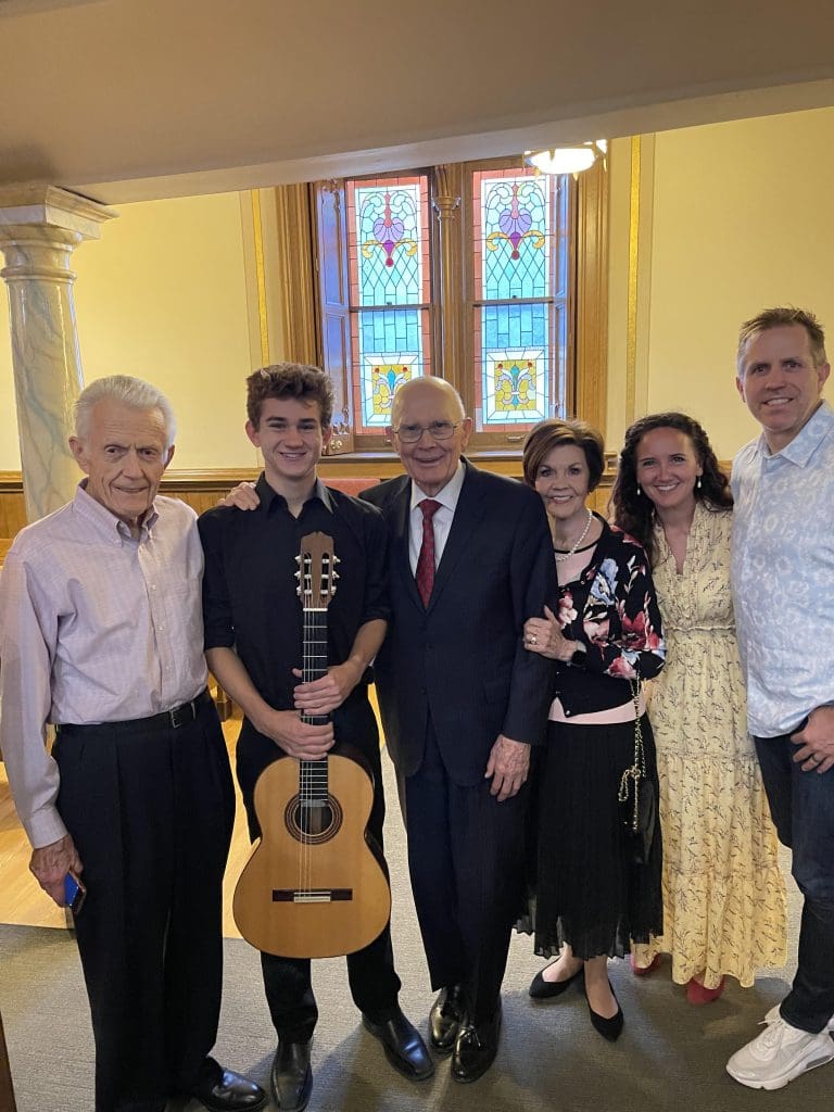 President Dallin H. Oaks celebrating a musical achievement with grandson and family, highlighting the legacy of work and testimony.
