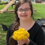 Grace Schara smiling and holding a bouquet of yellow dandelions in a backyard, representing the Grace Schara case and calls for a new trial.
