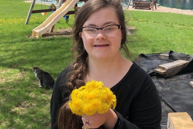 Grace Schara smiling and holding a bouquet of yellow dandelions in a backyard, representing the Grace Schara case and calls for a new trial.