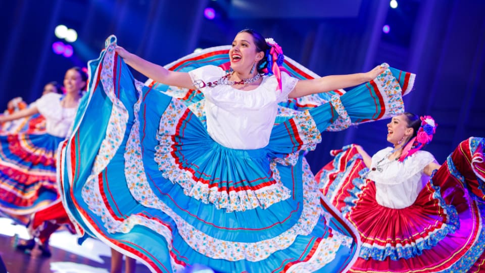 Performers in colorful traditional dresses dancing at Luz de las Naciones 2025, celebrating Latino culture and faith at the Conference Center in Salt Lake City.