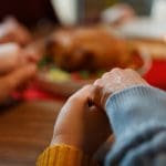 Family holding hands in prayer over a Thanksgiving meal, expressing gratitude and religious freedom as discussed in the article “Thanksgiving with New Perspective.”