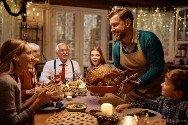 Family gathered around a Thanksgiving table as a man serves turkey, illustrating gratitude and themes from the hymn Thou Gracious God Whose Mercy Lends.
