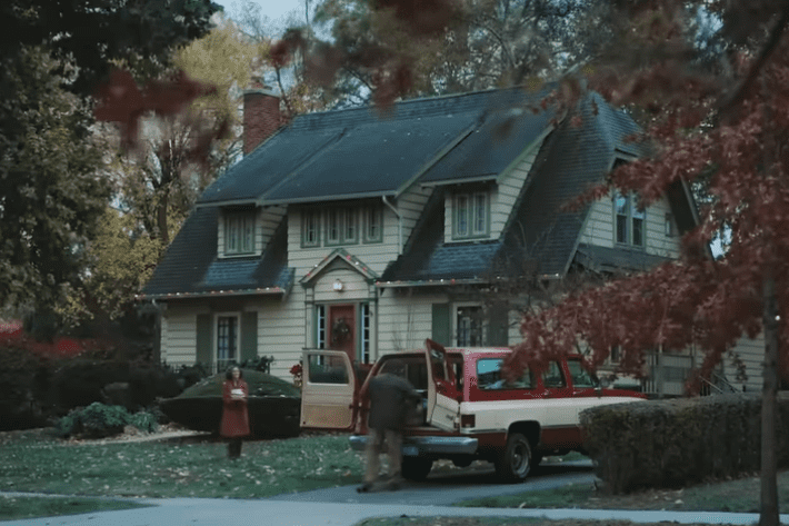 Family unloading gifts outside a decorated home in a nostalgic Christmas commercial scene
