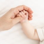 Adult hand holding a newborn baby’s hand, symbolizing abortion as a human rights violation and the protection of unborn life.