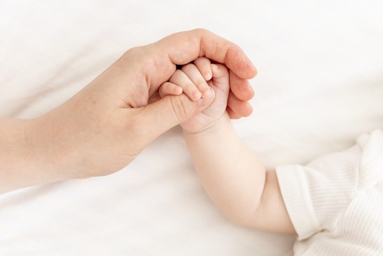 Adult hand holding a newborn baby’s hand, symbolizing abortion as a human rights violation and the protection of unborn life.