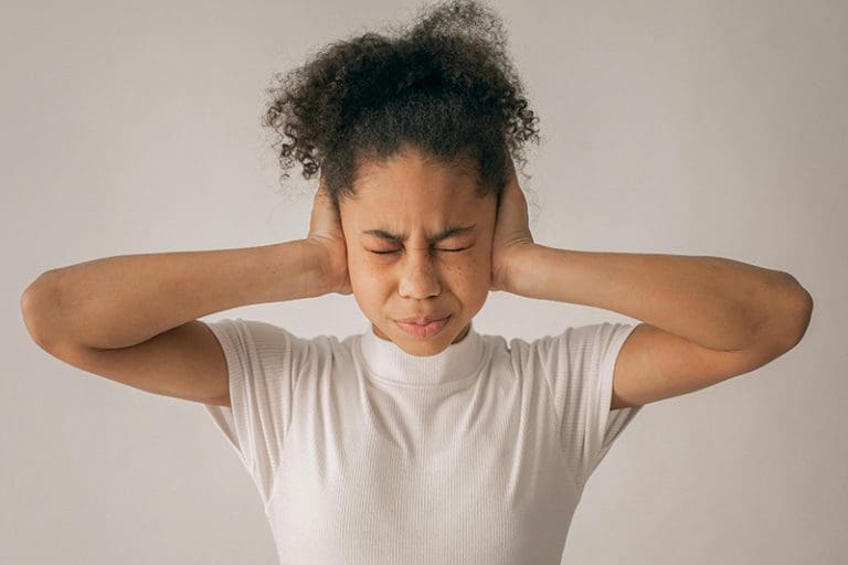 Girl covering her ears with eyes shut, illustrating C. S. Lewis’s The Last Battle metaphor about critics of the Church refusing to hear truth.