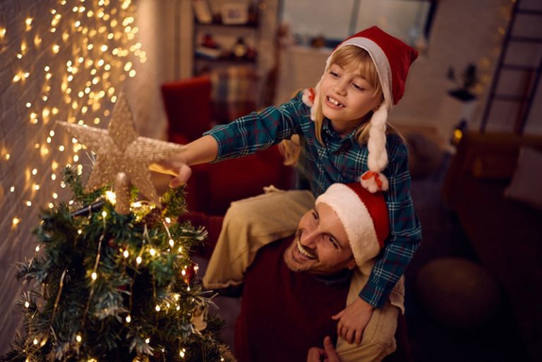 Father and child placing a star on a Christmas tree symbolizing the night without darkness and the hope and light of Jesus Christ at Christmas.