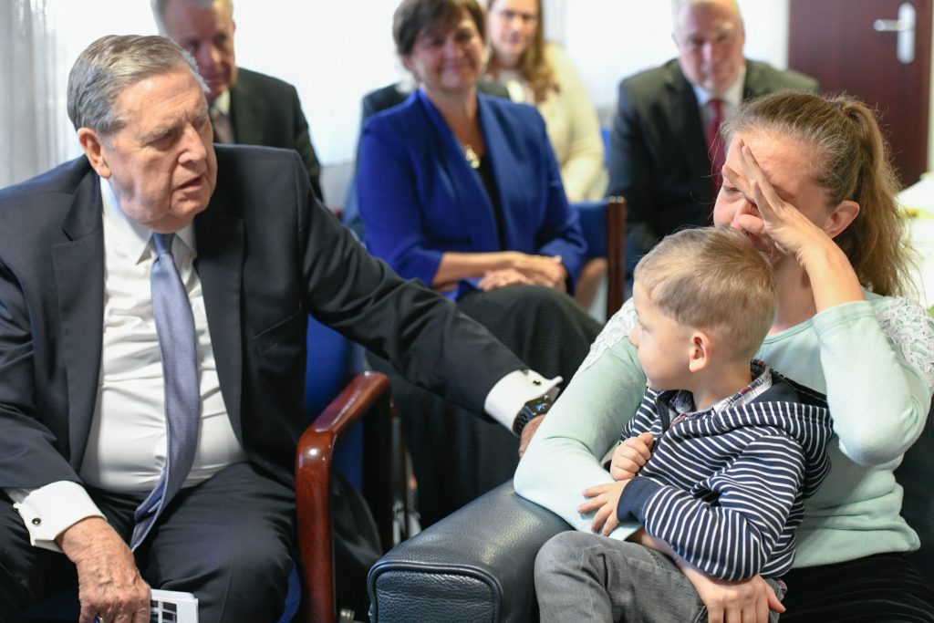 President Jeffrey R. Holland offers comfort and compassion to a mother and child, reflecting his Christlike ministry and deep empathy for those who suffer.