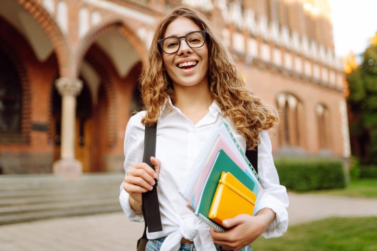 Student holding books outside a university, representing the Education Fund empowering global Church members through education and self-reliance.