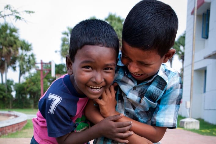 Two young boys laugh and embrace outdoors, capturing a spontaneous moment of joy, friendship, and connection between children.