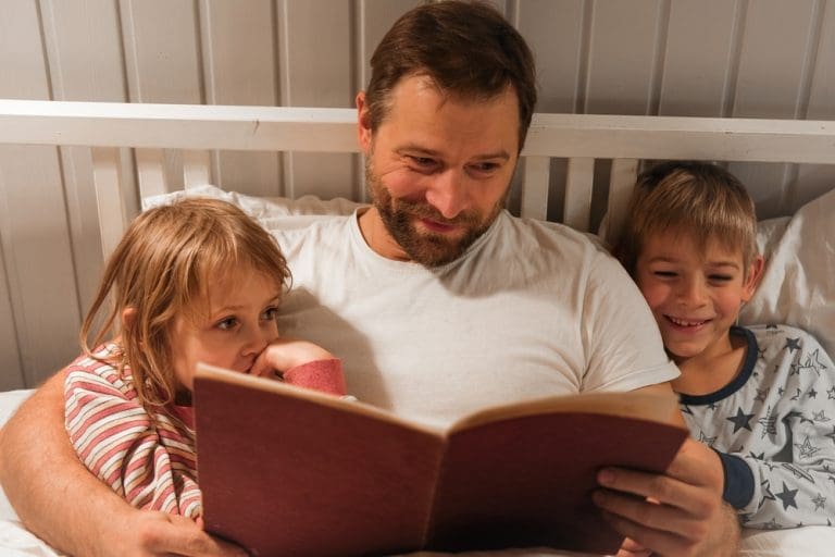 Father reading bedtime books aloud to two young children, highlighting the comfort and bonding of picture books and bedtime stories.