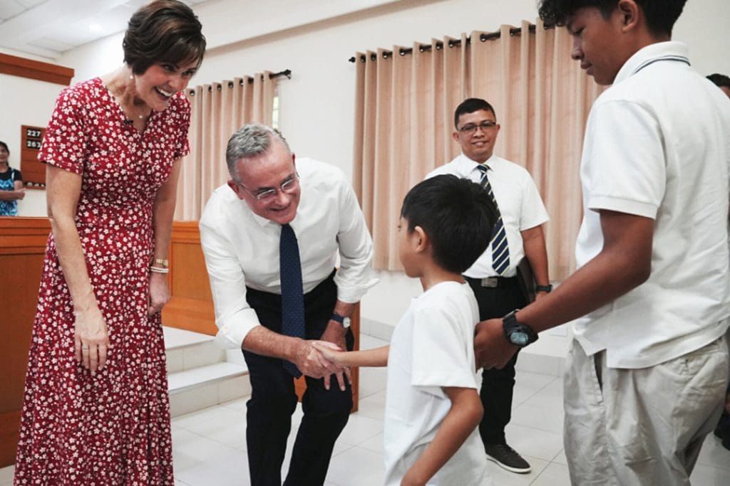 Elder Patrick Kearon and his wife, Jennifer Kearon, greet children and families at a Church gathering, reflecting their ministry within The Church of Jesus Christ of Latter-day Saints. The image supports the announcement of their participation in a global young adult devotional for young adults worldwide, commemorating the centennial of Institutes of Religion.