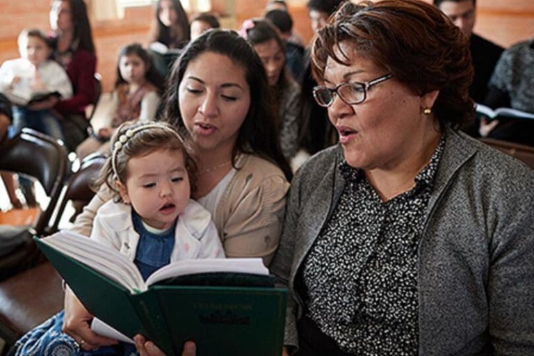Family singing from Hymns for Home and Church hymnbook during worship in The Church of Jesus Christ of Latter-day Saints.