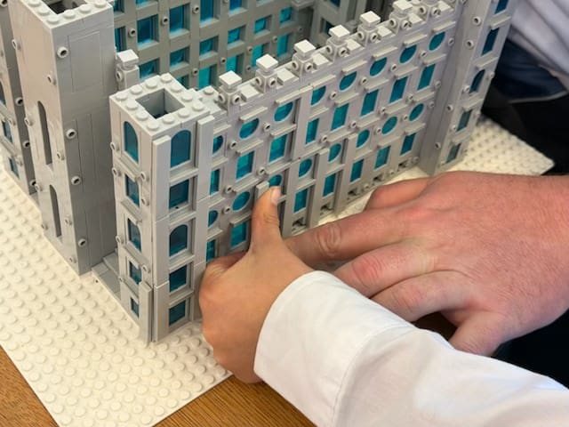 A child placing a brick onto the Lego-style Salt Lake Temple model, illustrating how the Temple can unite a Ward Family across generations.
