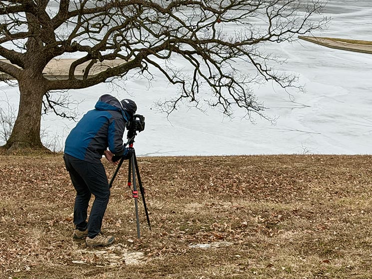 A filmmaker captures winter footage along an ice-lined river during the Joseph Smith Documentaries Project, reflecting the harsh conditions early Latter-day Saints endured.