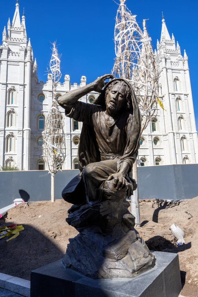 A statue of Jesus Christ in Gethsemane sits on the south side of Temple Square with the Salt Lake Temple behind it, inviting quiet reflection during the Easter season.