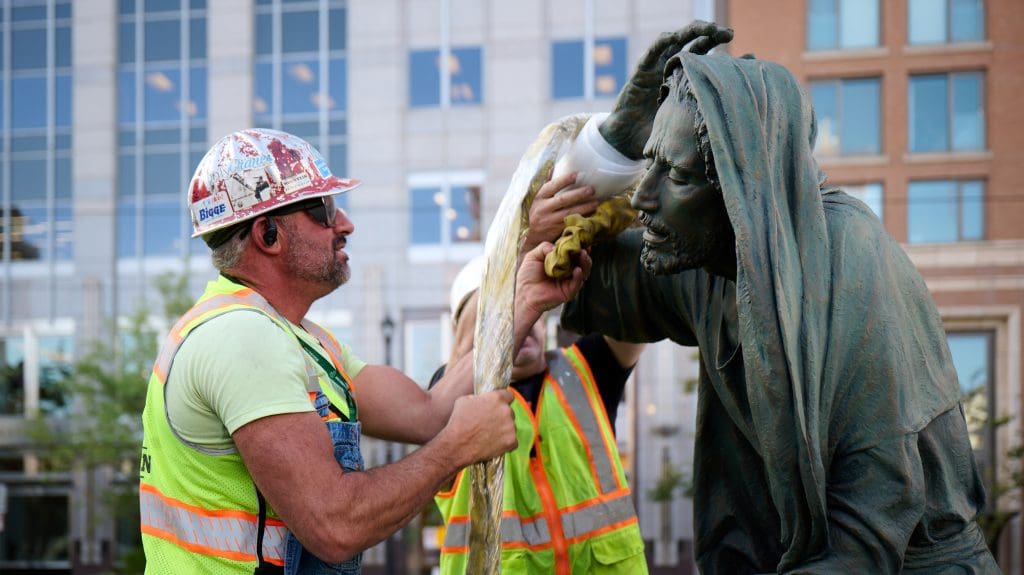 Workers carefully install a Jesus Christ statue at Temple Square near the Salt Lake Temple, preparing the sacred artwork for Easter season reflection on the Savior’s sacrifice.