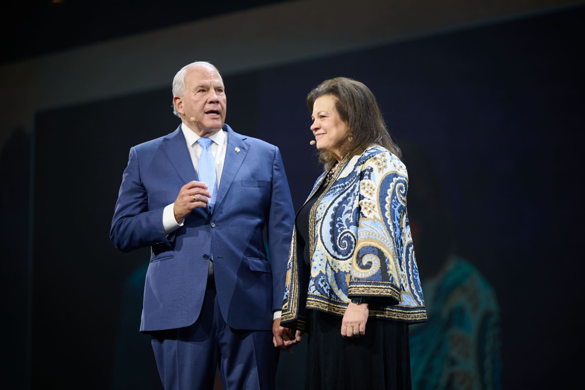 Elder Ronald A. Rasband of the Quorum of the Twelve Apostles and his wife Melanie speak on stage during Family Discovery Day at RootsTech 2026, sharing family history stories and encouraging families to build a legacy of faith.