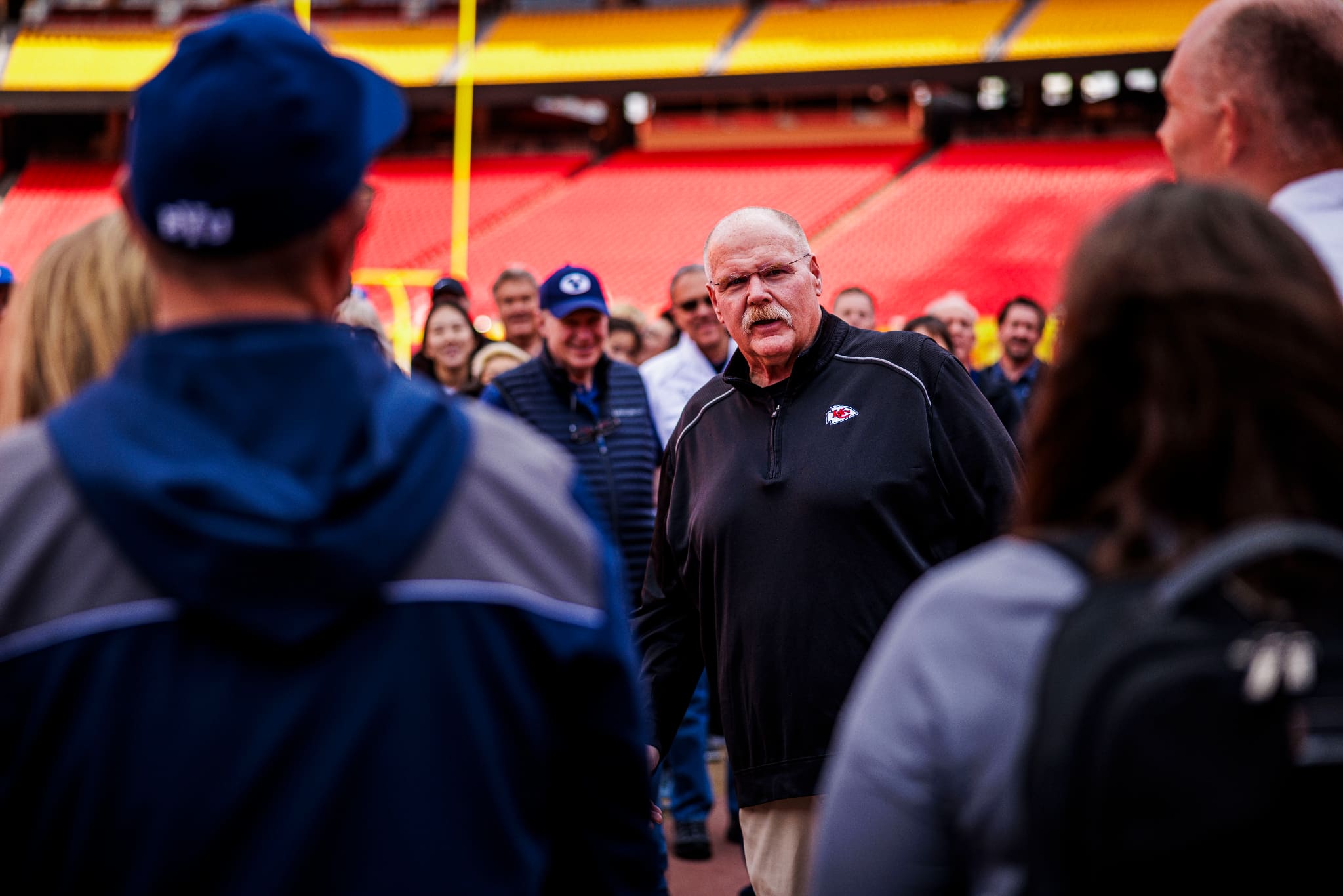 Andy Reid, Kansas City Chiefs head coach, speaks with a group on the field, highlighting his role as guest narrator for the Tabernacle Choir at Temple Square’s Music and the Spoken Word broadcast.