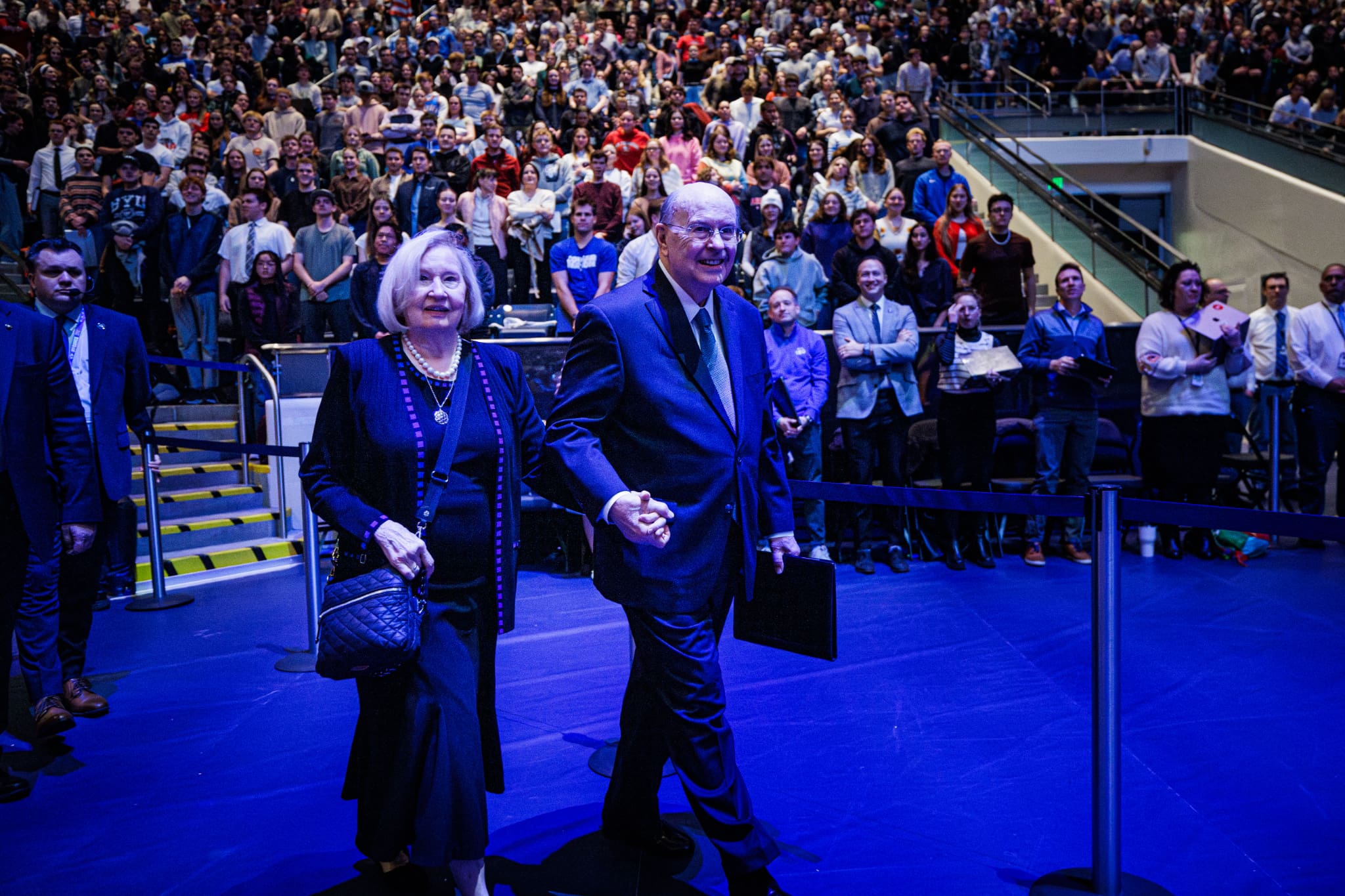 Elder Quentin L. Cook and his wife walk into the Marriott Center at Brigham Young University as thousands of BYU students gather for a devotional where he taught about faith, technology, and the challenges of the artificial intelligence age.