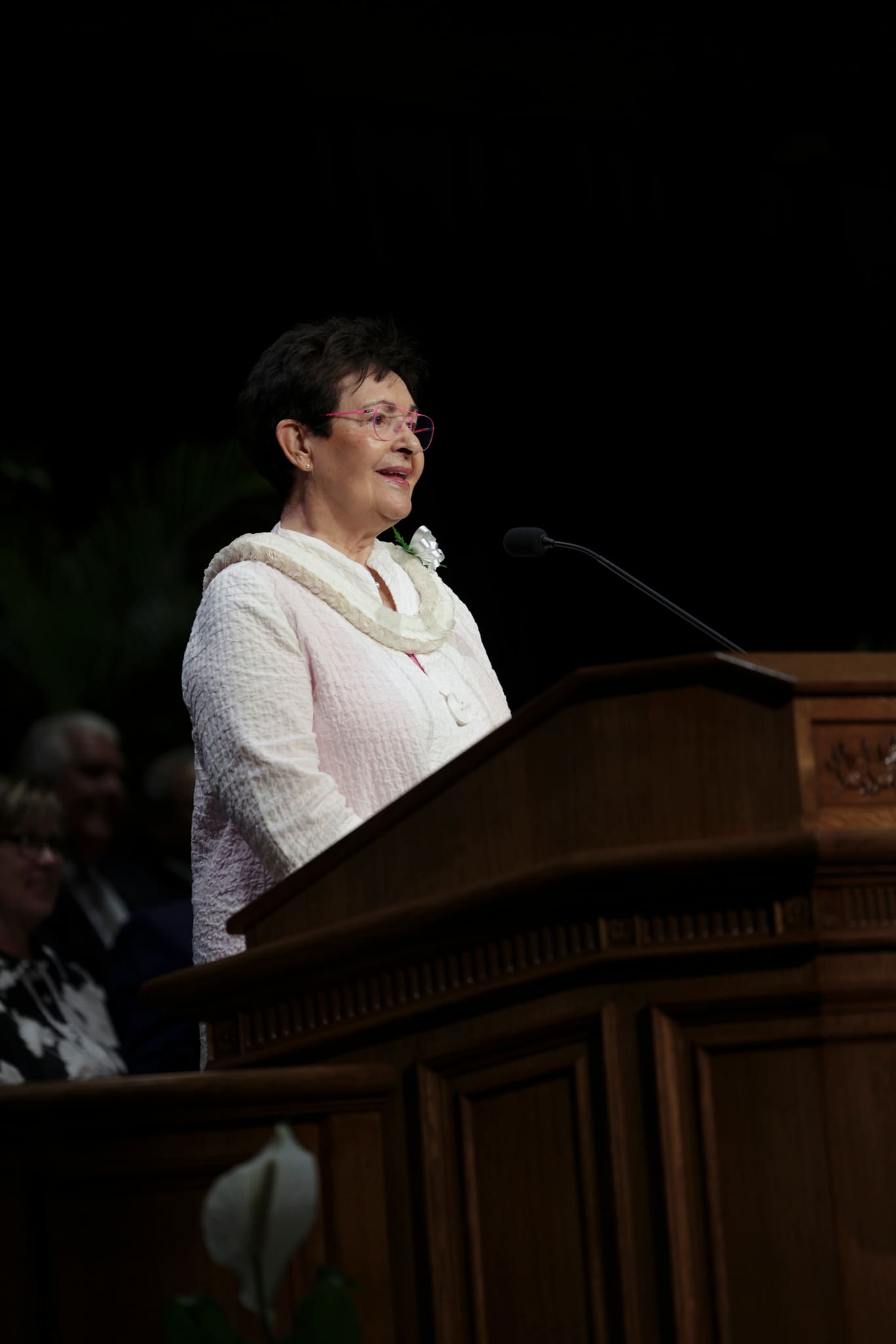 Sister Harriet Uchtdorf speaks from the pulpit during a BYU–Hawaii devotional alongside President Dieter F. Uchtdorf, encouraging faith and unity among young disciples of Jesus Christ.