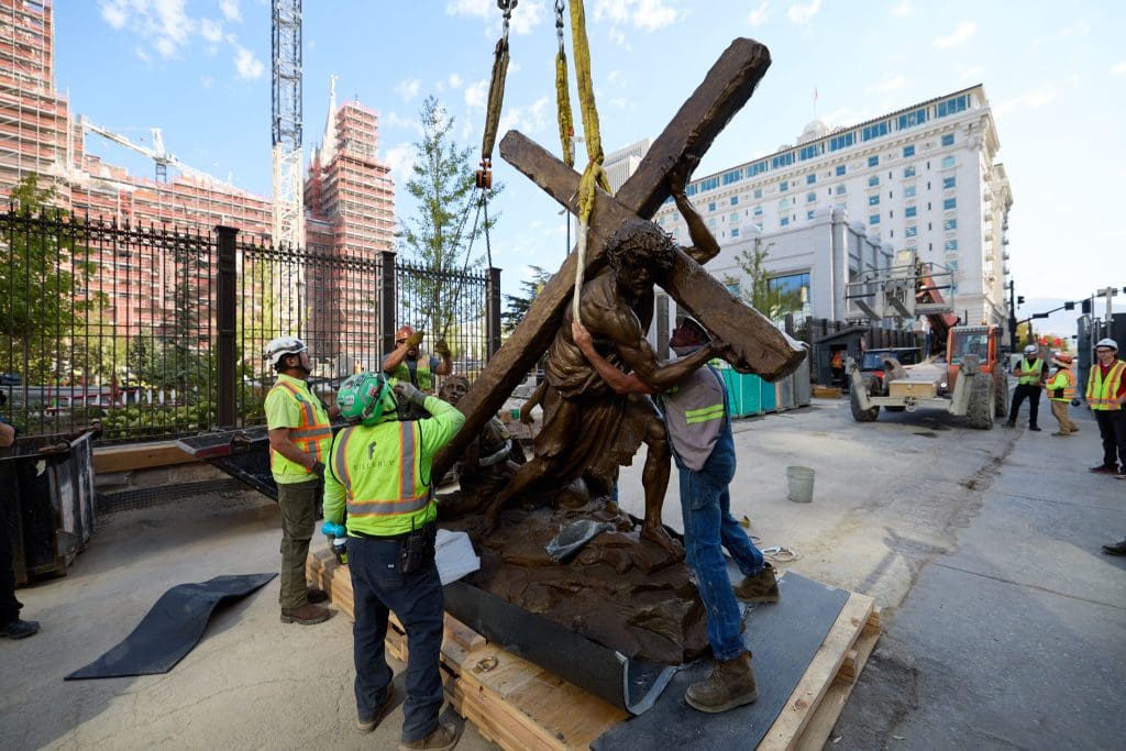 Construction crews position a large Jesus Christ statue carrying the cross at Temple Square near the Salt Lake Temple, highlighting the Easter season focus on Calvary.