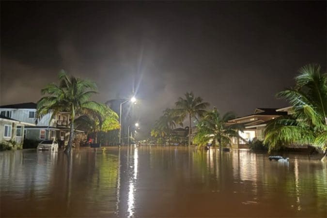 Severe flooding in a residential neighborhood in the Hawaiian Islands, showing homes surrounded by water during disaster response efforts.