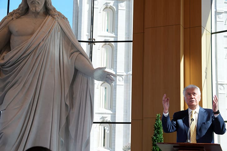 Christus statue inside the Temple Square Visitors’ Center with a Dieter F. Uchtdorf speaking, highlighting the central focus on Jesus Christ and temple teaching.
