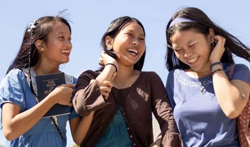 Three young women smiling and walking together, representing the new Young Women age-group names focused on faith, hope, and light.