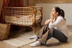 Exhausted young mother sitting beside a baby bassinet reflecting the challenges of motherhood, parenting struggles, and family life.