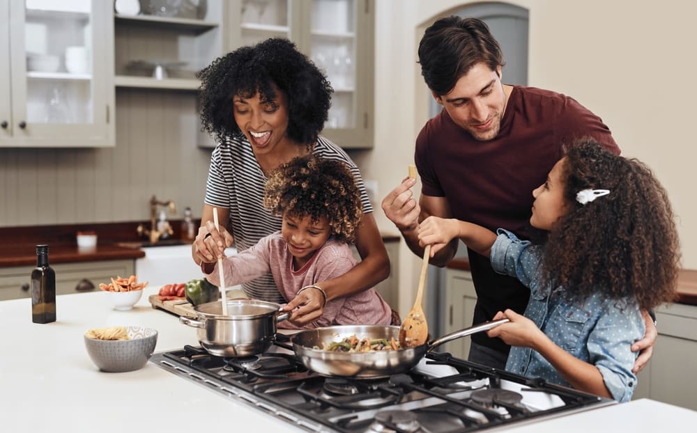 Family cooking together at home during a summer staycation, enjoying family activities and family bonding while building self-reliance.