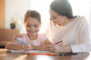 Mother and daughter using activity books and creative learning materials together, building critical-thinking skills and enjoying educational family fun.
